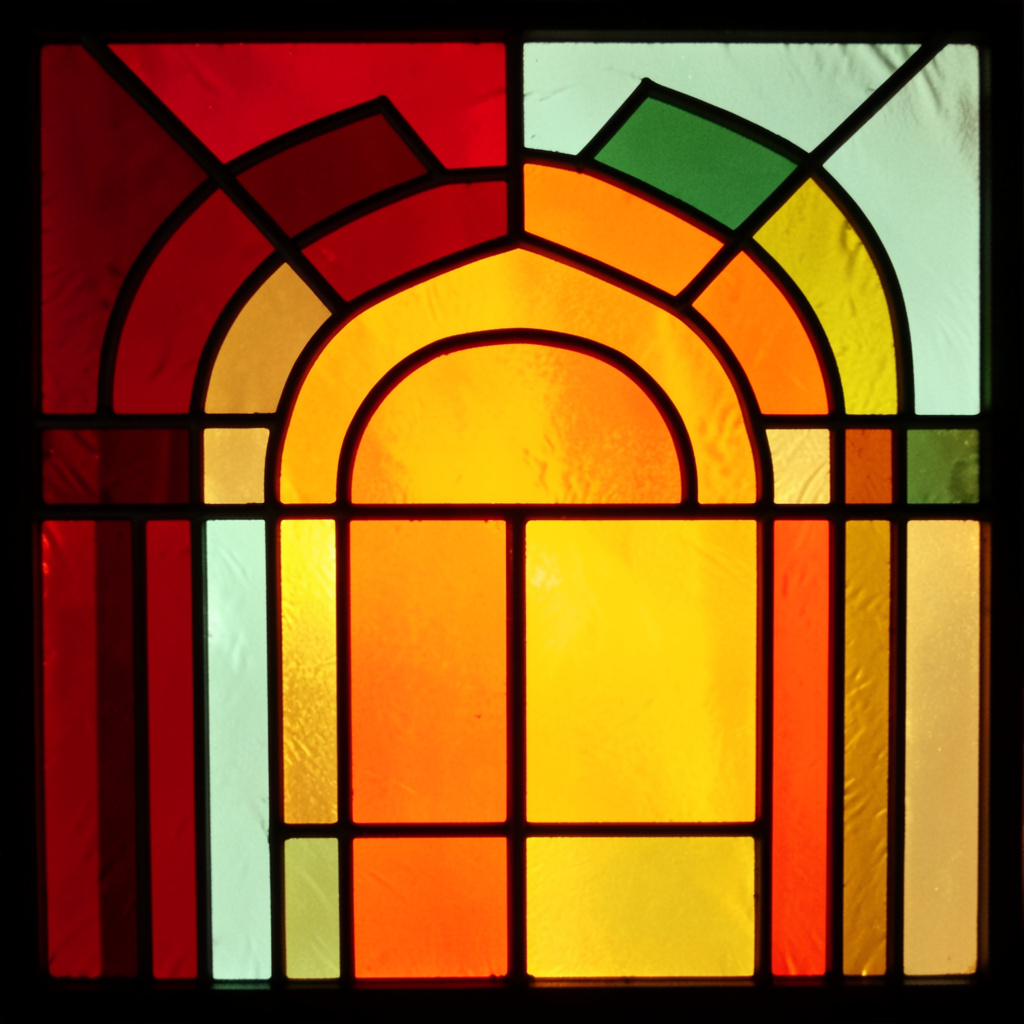 A stained-glass composition with bold leaded segments in crimson red, sage green, and golden yellow, forming an abstract playful arcade-inspired pattern